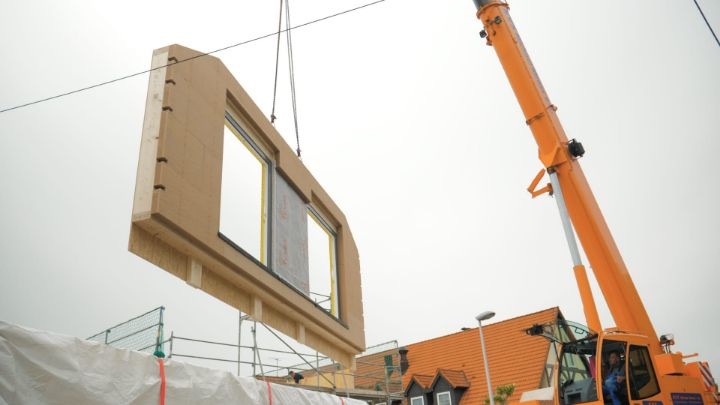 Vorgefertigtes Holzrahmen-Wandelement mit Fenster hängt am Kran über der Baustelle in Moritzburg