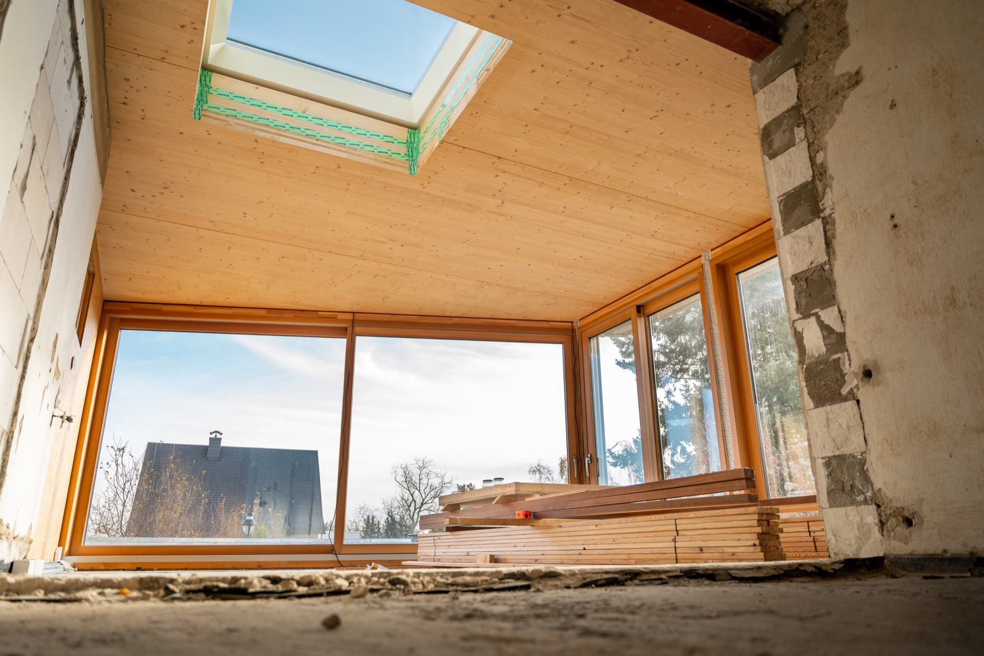 Innenraum des Holz-Anbaus im Rohbau mit Vollholzdecke, Dachfenster und raumhohen Fenstern